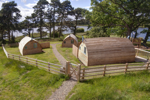 Houten pods bij Blackcleugh Glamping in het Verenigd Koninkrijk, omgeven door gras en hekwerk aan een meer.