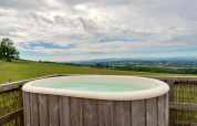 Outdoor hot tub overlooking scenic countryside at Bramble Yurt in the UK, set under a cloudy sky