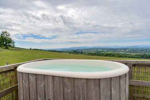 Outdoor hot tub overlooking scenic countryside at Bramble Yurt in the UK, set under a cloudy sky