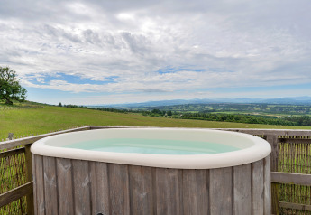 Außenwhirlpool mit Blick auf grüne Felder bei Bramble Yurt im Vereinigten Königreich unter bewölktem Himmel