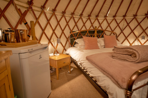 Interno accogliente di Bramble Yurt nel Regno Unito con letto matrimoniale, minibar e coperte morbide.