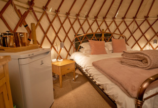 Interno accogliente di Bramble Yurt nel Regno Unito con letto matrimoniale, minibar e coperte morbide.