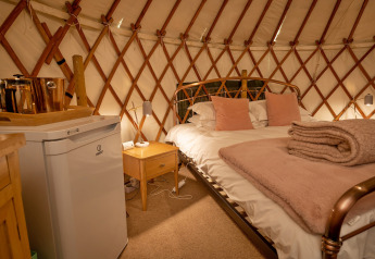 Gezellig interieur van Bramble Yurt in het VK met tweepersoonsbed, minikoelkast en zachte dekens.