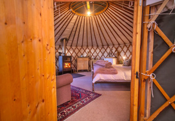 Interieur van de Bramble Yurt in het Verenigd Koninkrijk met comfortabel bed, houtkachel en warme sfeer.