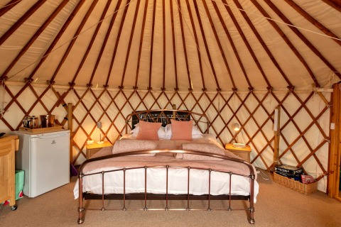 Indretning af Bramble Yurt i Storbritannien med dobbeltseng, natborde og minikøleskab.