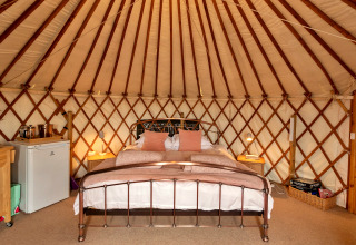 Indretning af Bramble Yurt i Storbritannien med dobbeltseng, natborde og minikøleskab.