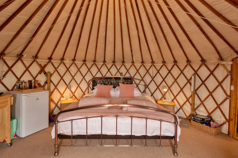 Interno di Bramble Yurt nel Regno Unito con letto matrimoniale, comodini e mini-frigo.