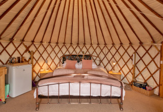 Interno di Bramble Yurt nel Regno Unito con letto matrimoniale, comodini e mini-frigo.
