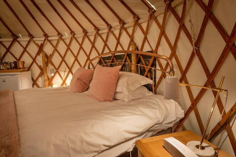 Letto accogliente con cuscini rosa in Bramble Yurt, Regno Unito, struttura in legno e luce calda.