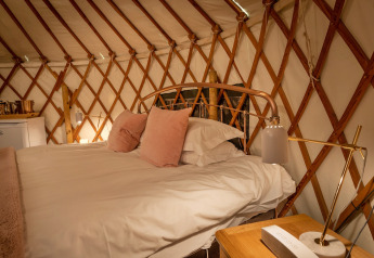 Knus bed met roze kussens in Bramble Yurt, Verenigd Koninkrijk, houten wanden en warme verlichting.