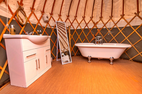Indretning af et badeværelse i en yurt med badekar, håndvask og spejl ved Bramble Yurt i Storbritannien.