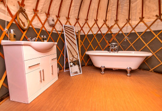 Indretning af et badeværelse i en yurt med badekar, håndvask og spejl ved Bramble Yurt i Storbritannien.