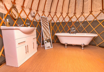 Badkamer in de Bramble Yurt in het Verenigd Koninkrijk, met bad, wastafel en staande spiegel.