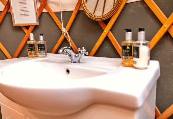 Modern sink with BeeKind soap and lotion bottles inside Bramble Yurt, UK, with cozy wooden decor.