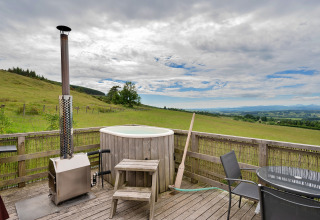 Terrazza esterna alla Bramble Yurt nel Regno Unito con vasca idromassaggio e vista sulle verdi colline.