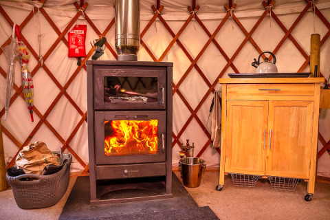 Indretning i Bramble Yurt i Storbritannien med brændeovn, tekande og træskab, varm og hyggelig stemning.