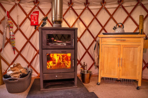 Interno della Bramble Yurt nel Regno Unito con stufa a legna, bollitore e mobile in legno, atmosfera accogliente.