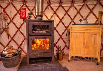Interieur van de Bramble Yurt in het Verenigd Koninkrijk met houtkachel, waterkoker en houten kast.