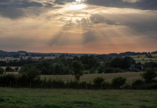 Landschapsfoto gemaakt bij een pod, met groene velden, bomen en zonnestralen door de wolken.