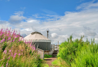Bramble Yurt in the United Kingdom, surrounded by wildflowers and greenery under a partly cloudy sky.