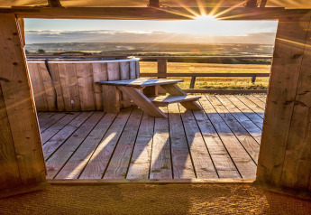 Blick aus der Bramble Yurt in Großbritannien auf eine Holzterrasse, Hot Tub und Sonnenuntergang.