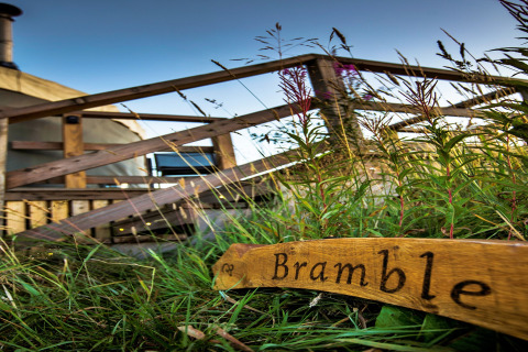 Photo of Bramble Yurt in the UK, featuring a wooden sign and outdoor steps leading up to the yurt entrance.