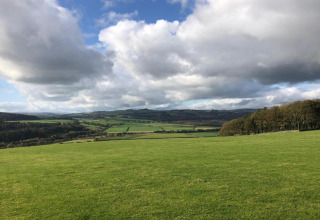 Landschapsfoto genomen bij een pod, met groene velden, glooiende heuvels, bomen en wolken in de lucht.