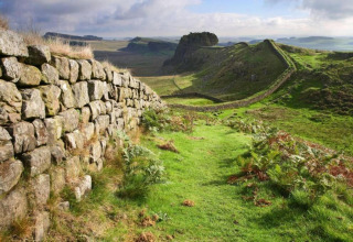 Een oude stenen muur slingert door een groen, heuvelachtig landschap onder een bewolkte hemel in Engeland.