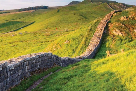 Foto van de Muur van Hadrianus, een oude stenen muur die door glooiende groene heuvels loopt.