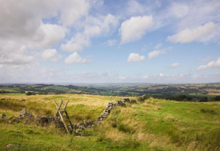Uitzicht op het groene Engelse platteland met een stenen muur en houten overstap onder blauwe lucht.