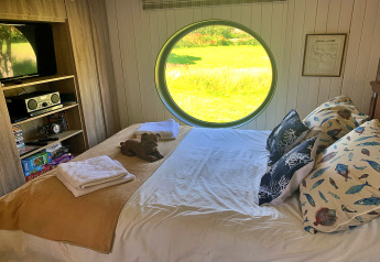 Camera da letto in Oak Tree Lodge, Regno Unito: finestra rotonda, letto matrimoniale e cuscini colorati.