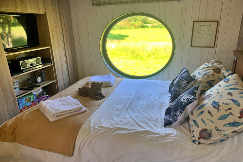Chambre d’Oak Tree Lodge au Royaume-Uni, grande fenêtre ronde, lit double, coussins à motifs animaliers.