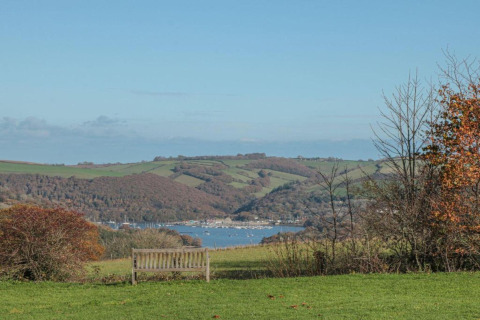 Banc avec vue sur les collines, la rivière et des bateaux près d'Oak Tree Lodge au Royaume-Uni, ciel bleu.