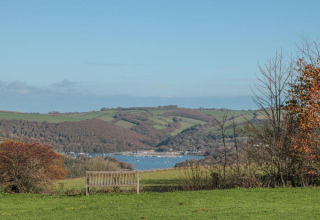 Banc avec vue sur les collines, la rivière et des bateaux près d'Oak Tree Lodge au Royaume-Uni, ciel bleu.