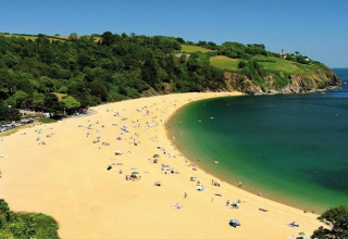 Plage de sable doré près d’Oak Tree Lodge au Royaume-Uni, entourée de collines vertes et d’une mer bleue.