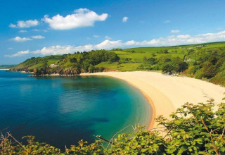 Vue depuis le mobil-home Oak Tree Lodge sur une baie de sable, mer bleue et champs verts au Royaume-Uni.