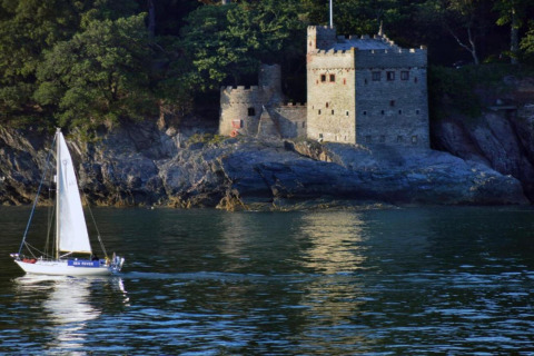Un voilier passe devant une maison-château en pierre, vue depuis Oak Tree Lodge au Royaume-Uni.