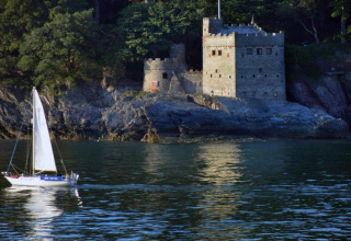 Un voilier passe devant une maison-château en pierre, vue depuis Oak Tree Lodge au Royaume-Uni.