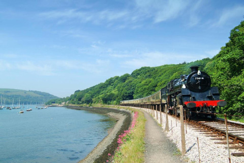 Un train à vapeur longe la rivière près d’Oak Tree Lodge au Royaume-Uni, entouré de collines verdoyantes.