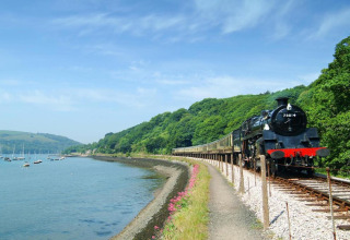 Un train à vapeur longe la rivière près d’Oak Tree Lodge au Royaume-Uni, entouré de collines verdoyantes.