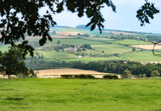 Uitzicht op glooiende groene velden en boerderijen in de verte, gezien vanaf een plekje bij een vijver.
