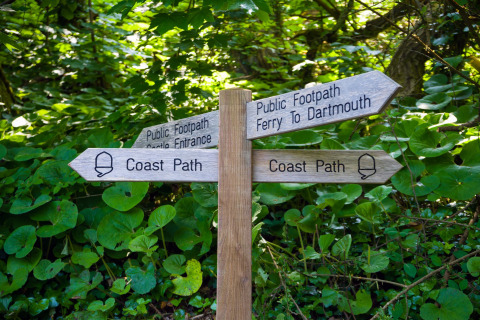 Panneau en bois indiquant la Coast Path, le ferry pour Dartmouth et l’entrée du château, dans la verdure.