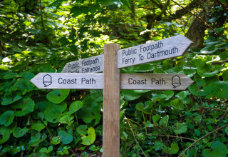 Panneau en bois indiquant la Coast Path, le ferry pour Dartmouth et l’entrée du château, dans la verdure.