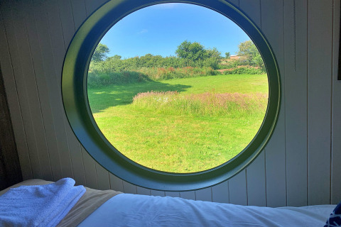 Vue depuis Oak Tree Lodge au Royaume-Uni à travers une fenêtre ronde sur un champ vert et ciel bleu.