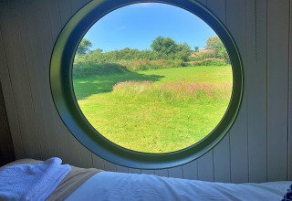 Vue depuis Oak Tree Lodge au Royaume-Uni à travers une fenêtre ronde sur un champ vert et ciel bleu.