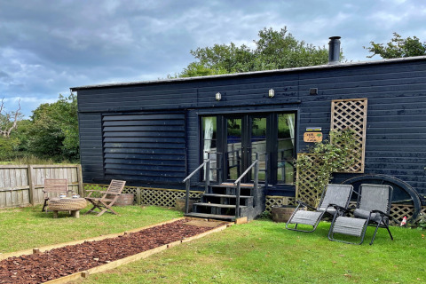 Mobil-home Oak Tree Lodge à façade noire, meubles de jardin, chaises longues et jardin verdoyant.