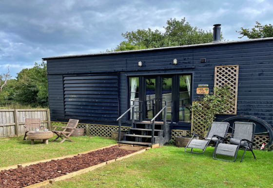 Mobil-home Oak Tree Lodge à façade noire, meubles de jardin, chaises longues et jardin verdoyant.