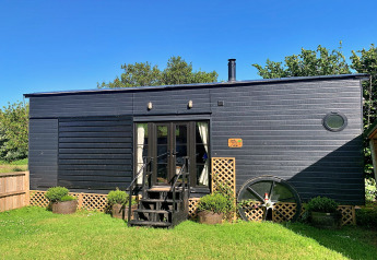 Casa mobile moderna nera chiamata Oak Tree Lodge con giardino e cielo blu, situata nel Regno Unito.