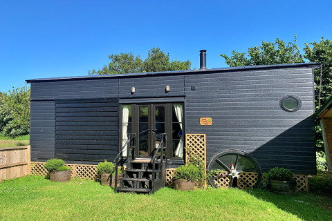 Mobil-home moderne noir nommé Oak Tree Lodge avec jardin vert et ciel bleu, situé au Royaume-Uni.