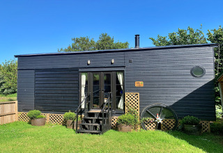 Mobil-home moderne noir nommé Oak Tree Lodge avec jardin vert et ciel bleu, situé au Royaume-Uni.
